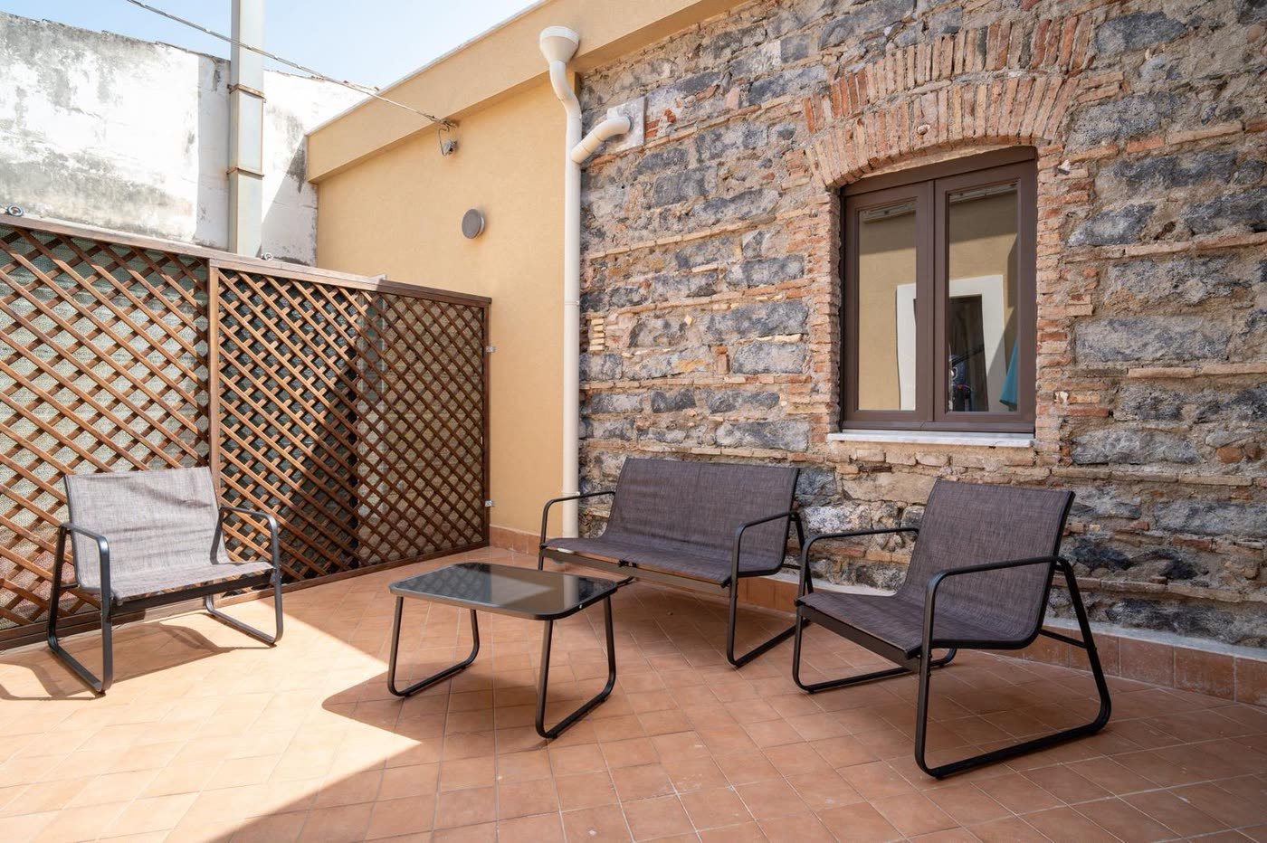 Al Ciclope — la terrazza con le poltrone e il muro in pietra lavica